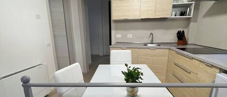 A modern kitchen with white cabinetry, a dining table with chairs, and a small potted plant.