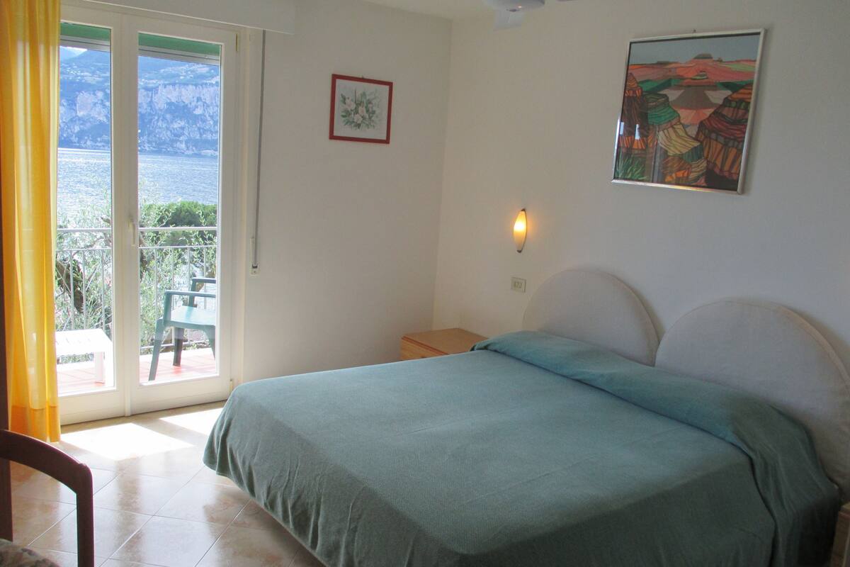 A bedroom with a bed, a nightstand, a window with a view of the outdoors, and a painting on the wall.