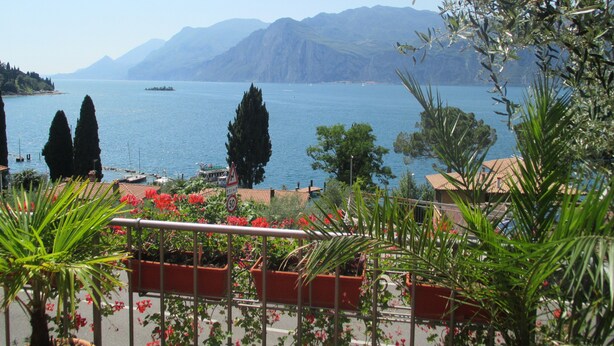 A coastal view with mountains in the background, a body of water, and potted plants in the foreground. - Casa Popi (Malcesine)