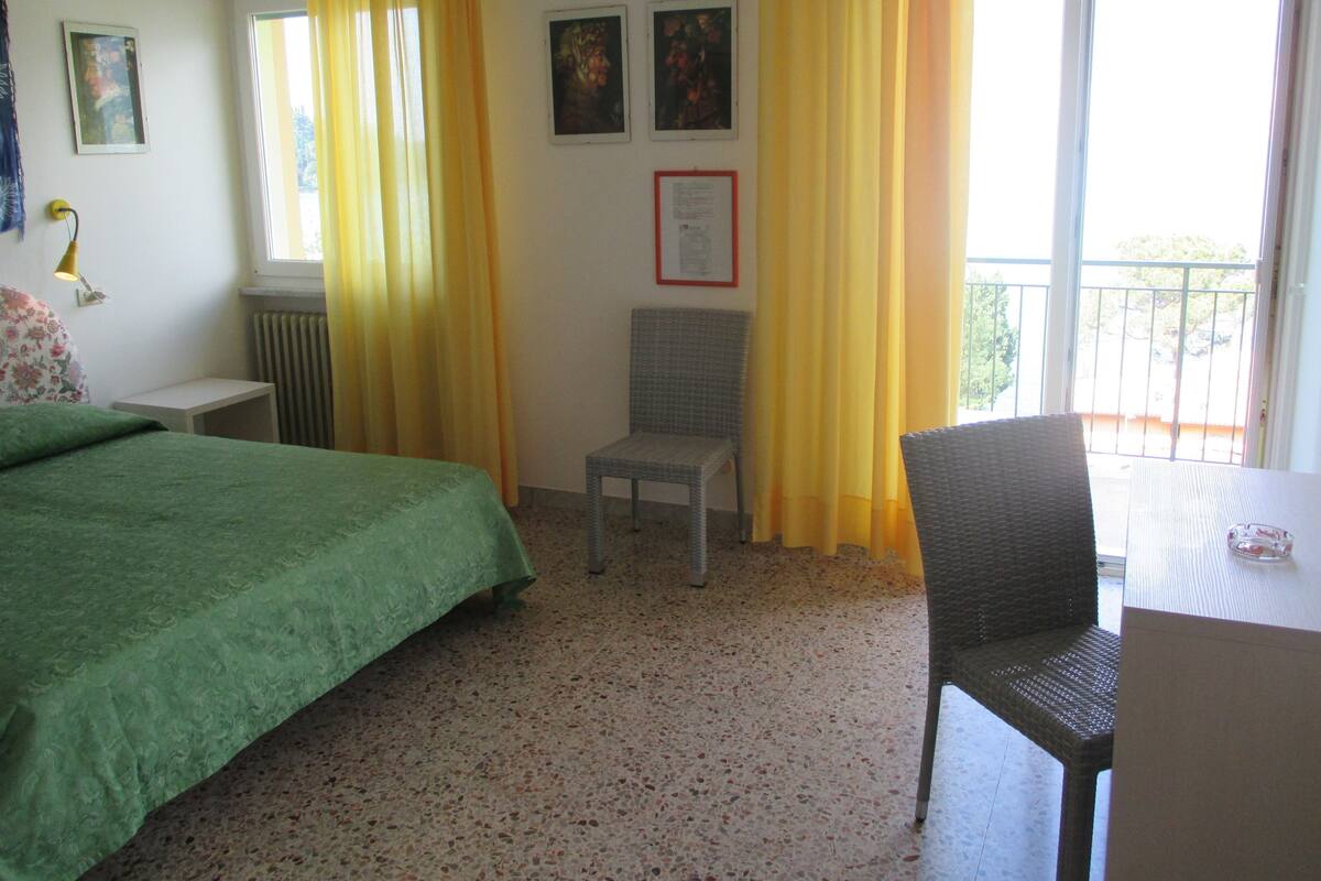A hotel room with a bed, a chair, a table, and a balcony with yellow curtains.