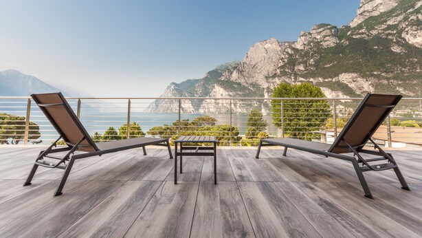 A wooden deck with two lounge chairs and a table, overlooking a mountainous coastline. - Bellariva (Riva del Garda)