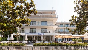 A restaurant with outdoor seating, a sign reading "Ristorante Pizzeria Bellaria," and a modern building in the background. - Bellariva (Riva del Garda)