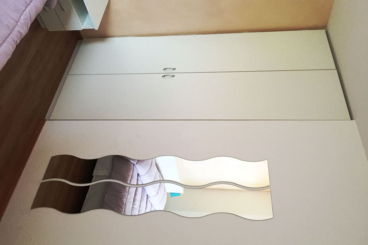 A bedroom with a bed, a wardrobe, and a mirror on the floor.