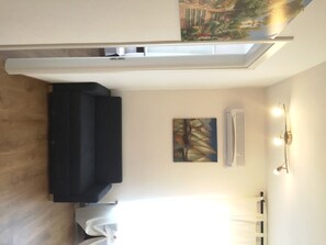 A room with a black sofa, a painting on the wall, a radiator, and a wall-mounted light fixture. - Bellariva (Riva del Garda)