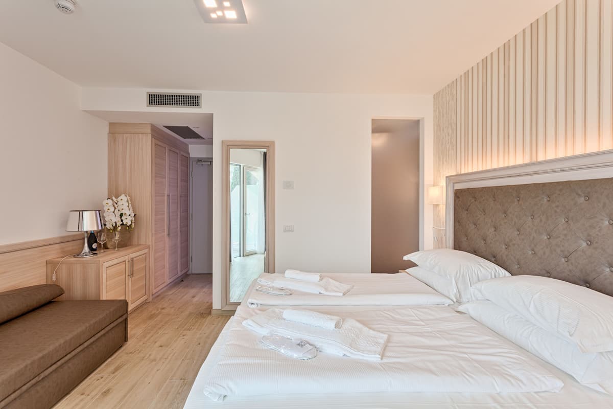 A hotel room with a large bed, a bedside table with a lamp, a wooden wardrobe, and a mirror.
