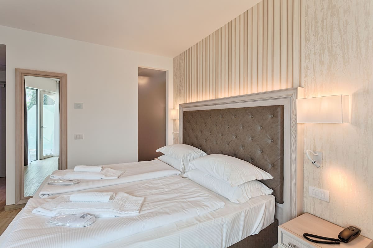 A hotel room with two beds, a large mirror, a bedside table with a lamp, and a telephone.