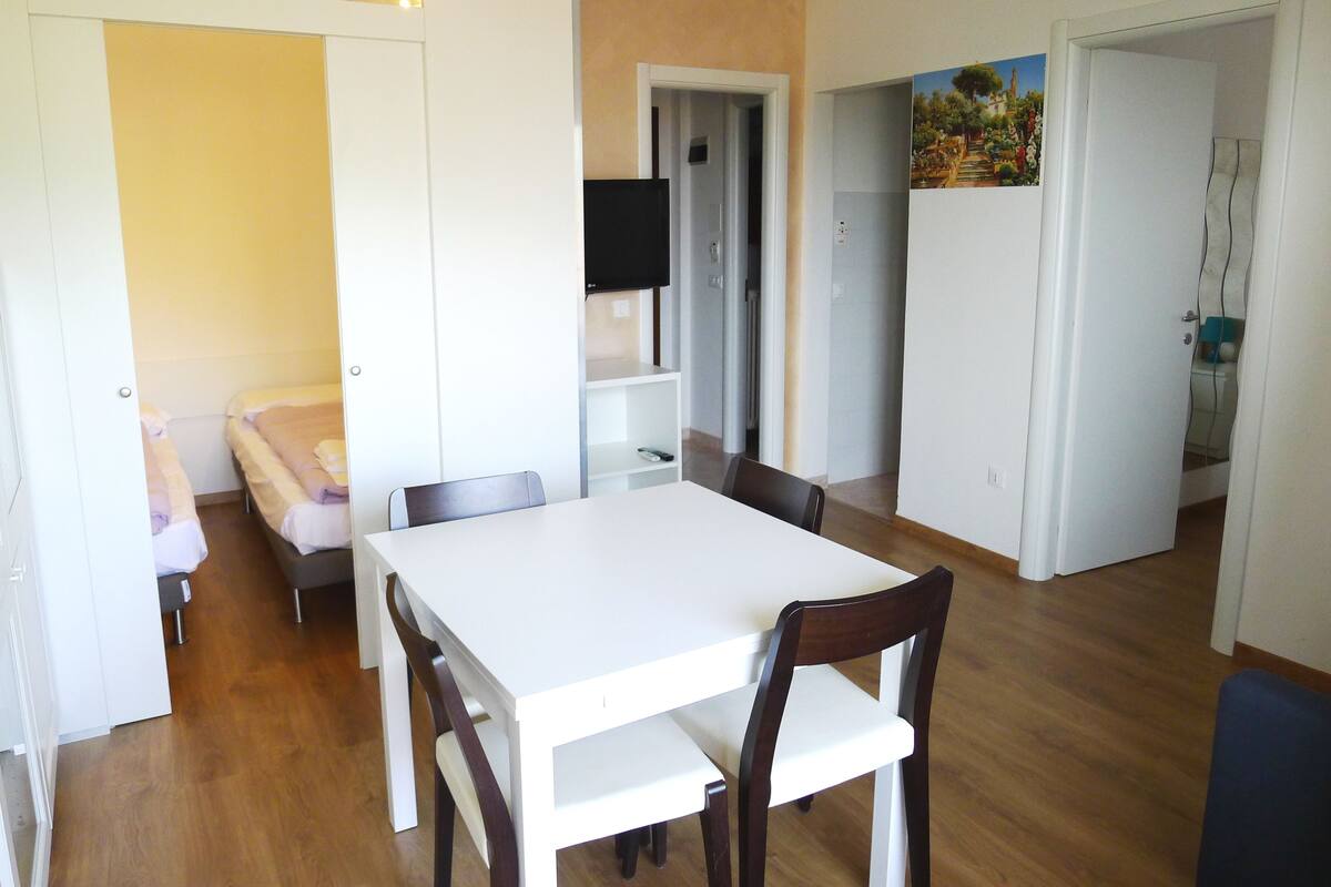 A compact living space with a dining table and chairs, a sofa, and a TV in the background.