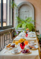 A breakfast table set with plates, cups, a muffin, a croissant, and a glass of orange juice.