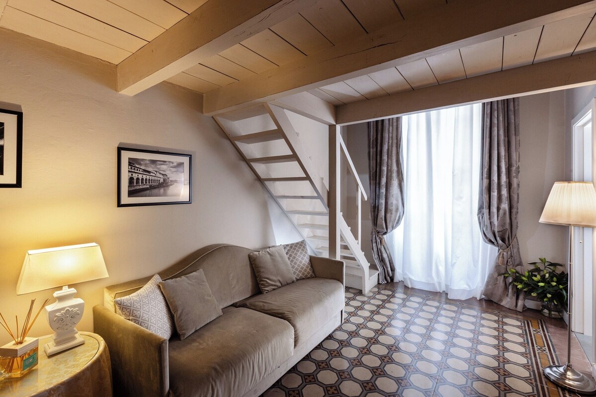 A cozy room with a sofa, a lamp, a picture on the wall, a staircase, and a patterned floor.