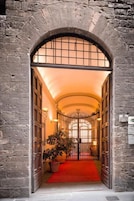 An arched entrance with a red carpet leading inside, stone walls, and a potted plant.