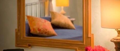 A hotel room with a bed, a bedside lamp, a laptop, a vase with flowers, and a mirror reflecting the room.