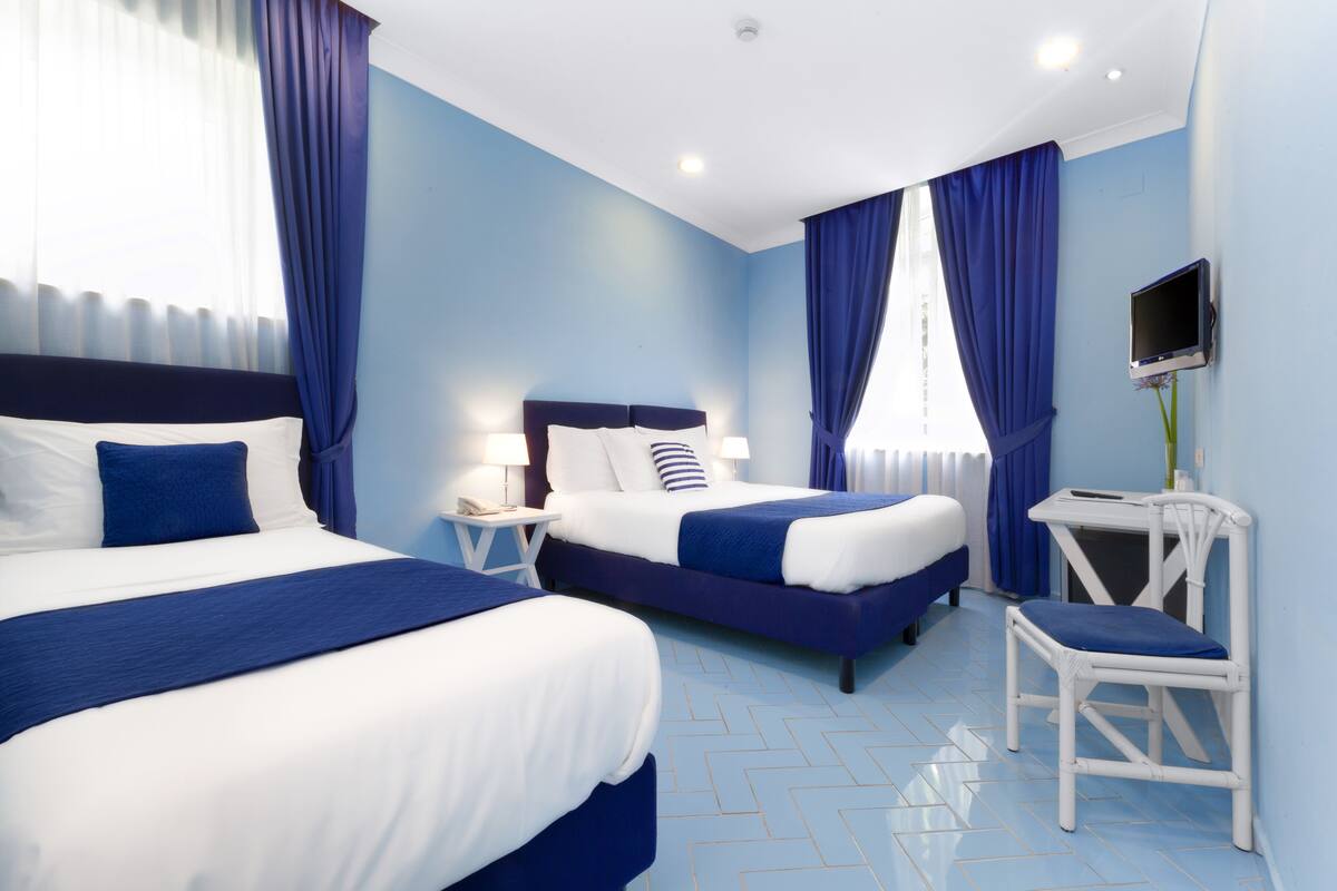 Habitació d'hotel amb dos llits, una taula de treball, una cadira i una televisió.