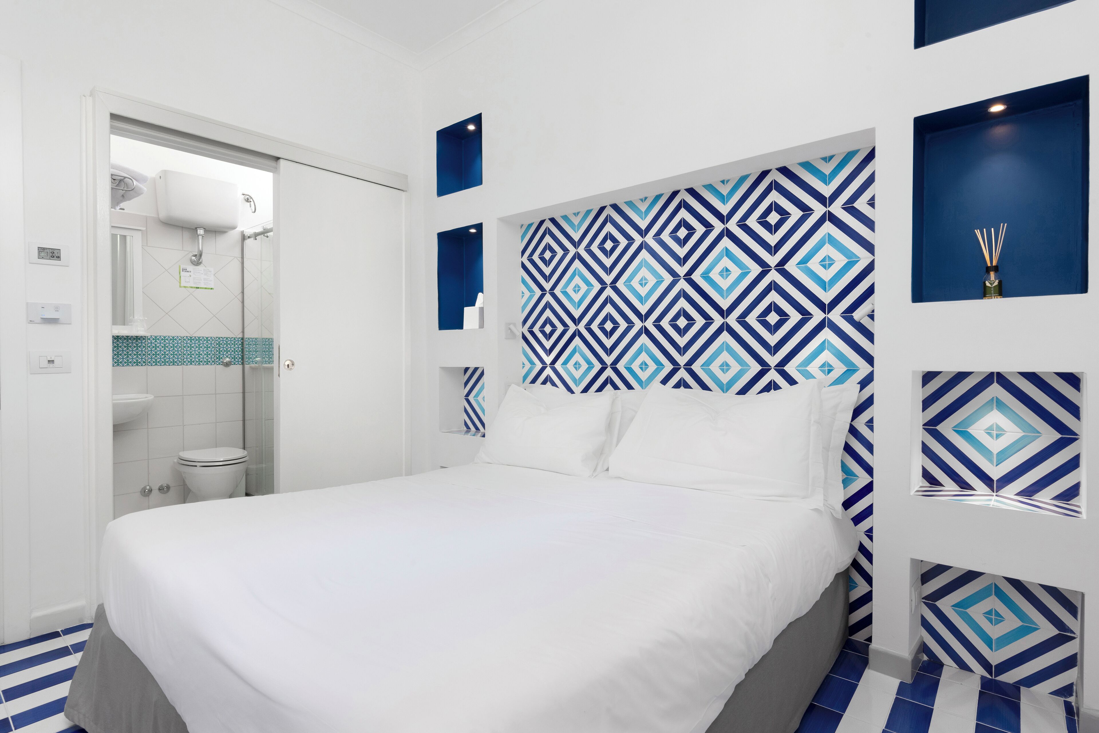 A modern hotel room with a large bed, a shower area, and a patterned wall.