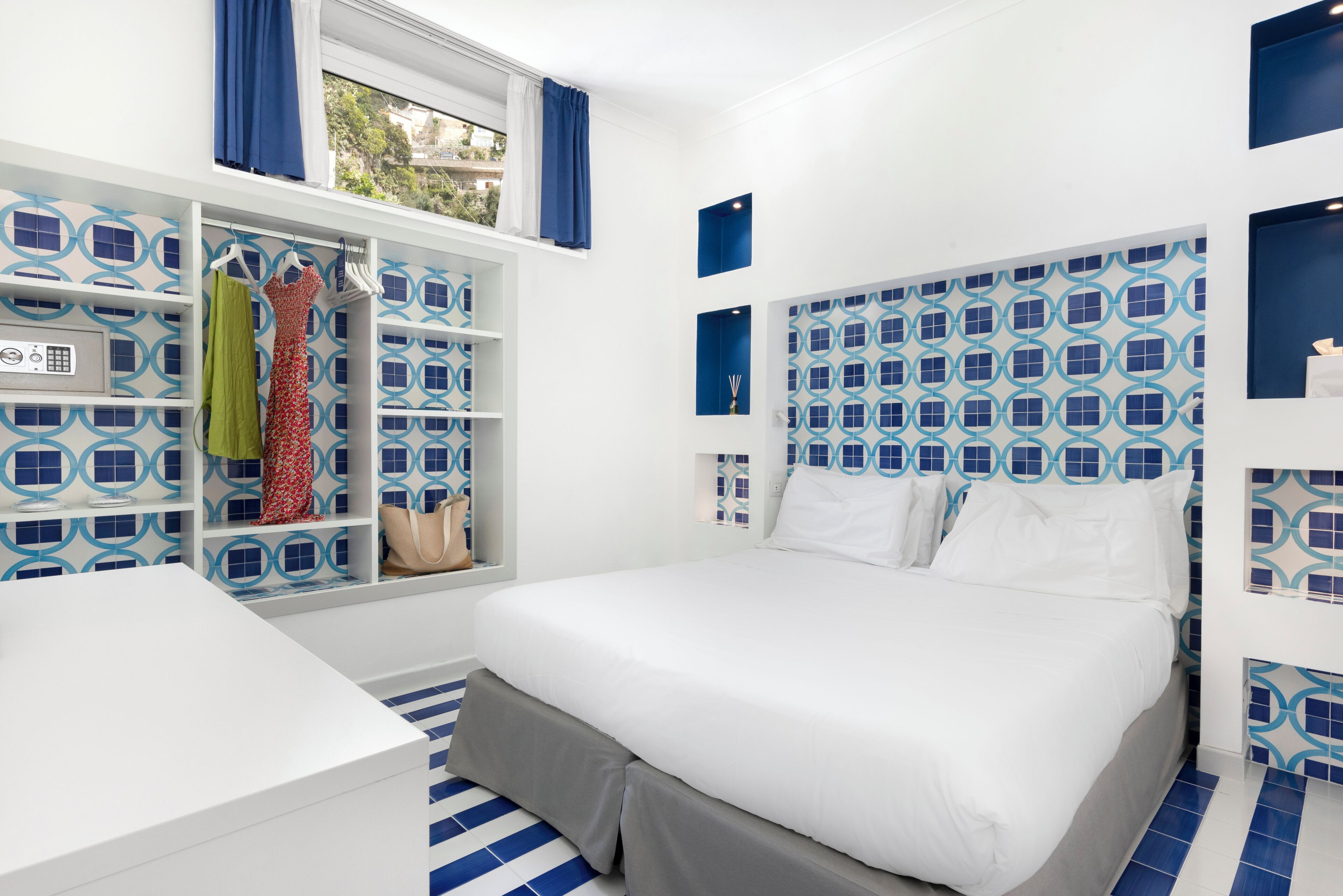 A hotel room with a bed, a wardrobe with hanging clothes, and a window with curtains.