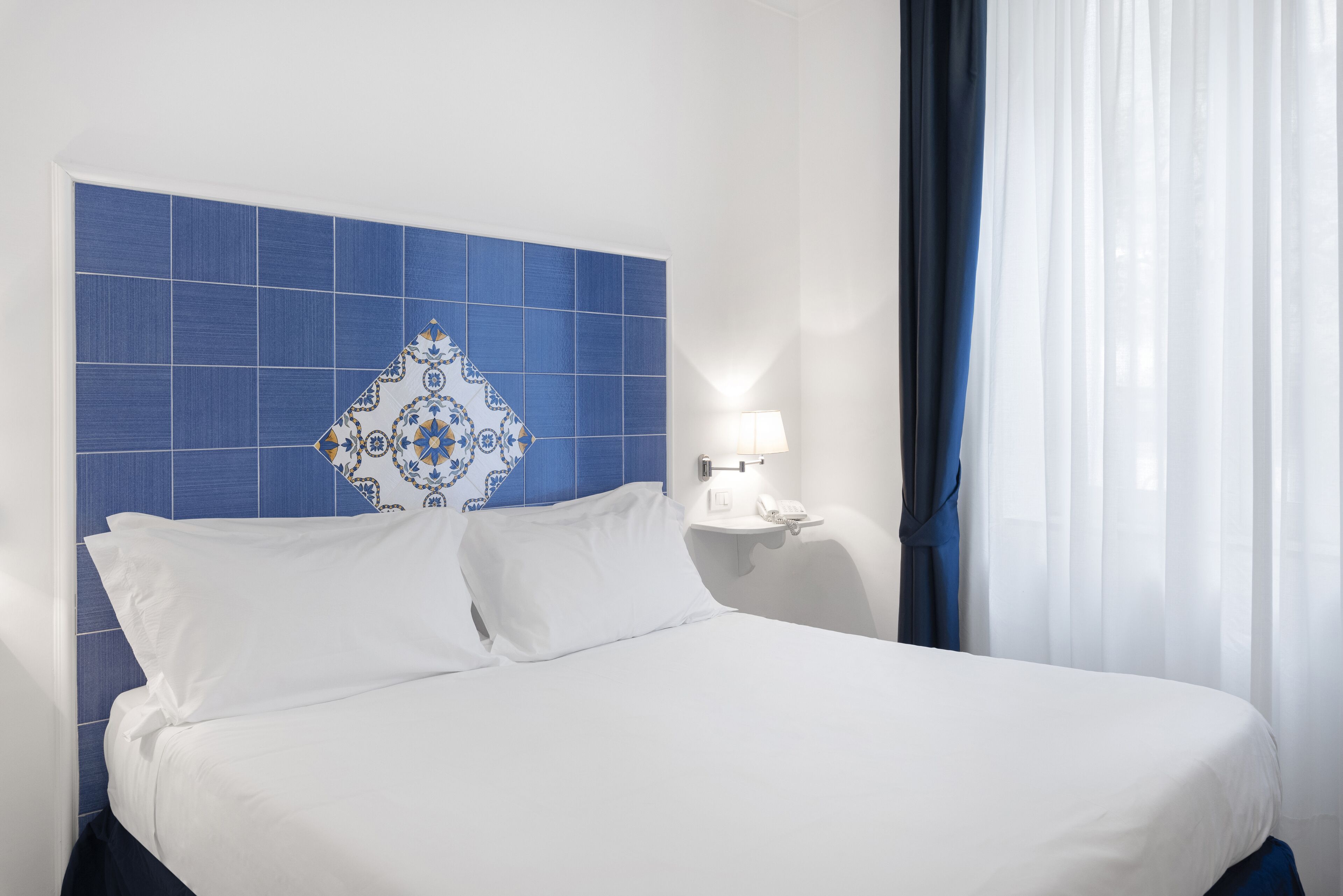 Ein Hotelzimmer mit einem großen Bett, einem Nachttisch mit Lampe und einem Kopfstück mit blau-weißem Muster.
