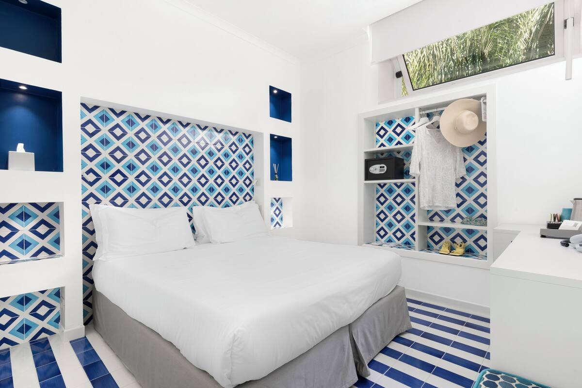 Habitació d'hotel moderna amb un llit gran, un taulell de tocador amb mirall i una finestra amb vista a palmeres.