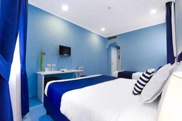 A hotel room with a bed, a desk, a chair, a television, and a door. - Hotel La Bougainville (Positano)
