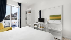 Habitació d'hotel amb un llit, un escriptori amb un ordinador, una televisió i una cadira. Hi ha un balcó amb vistes a edificis.
