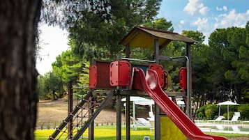 Children can play on the slide and climb the ladder in this park's play area surrounded by lush greenery and trees.