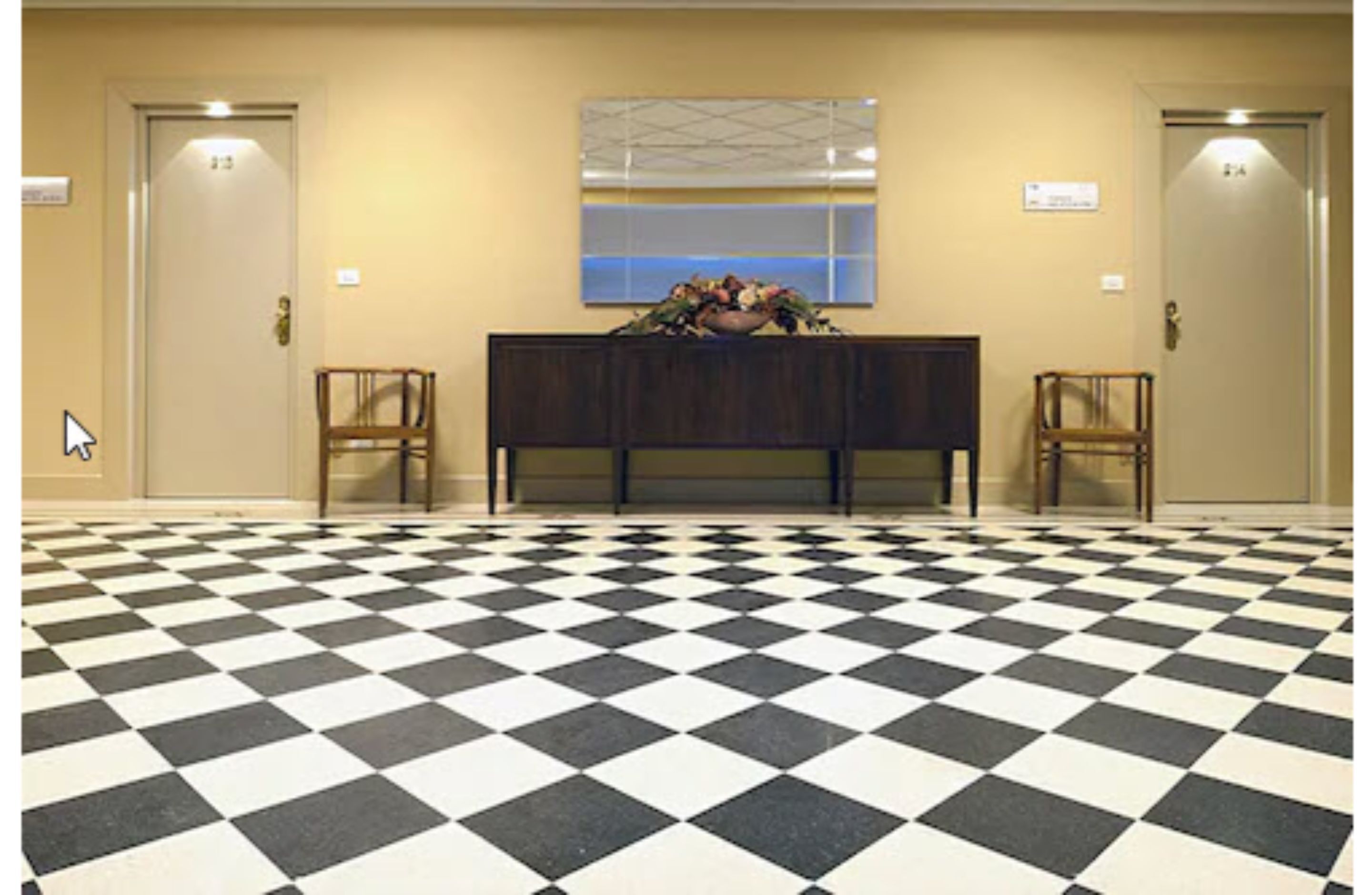 Un hall con suelo a cuadros, una recepción, dos sillas y dos puertas.