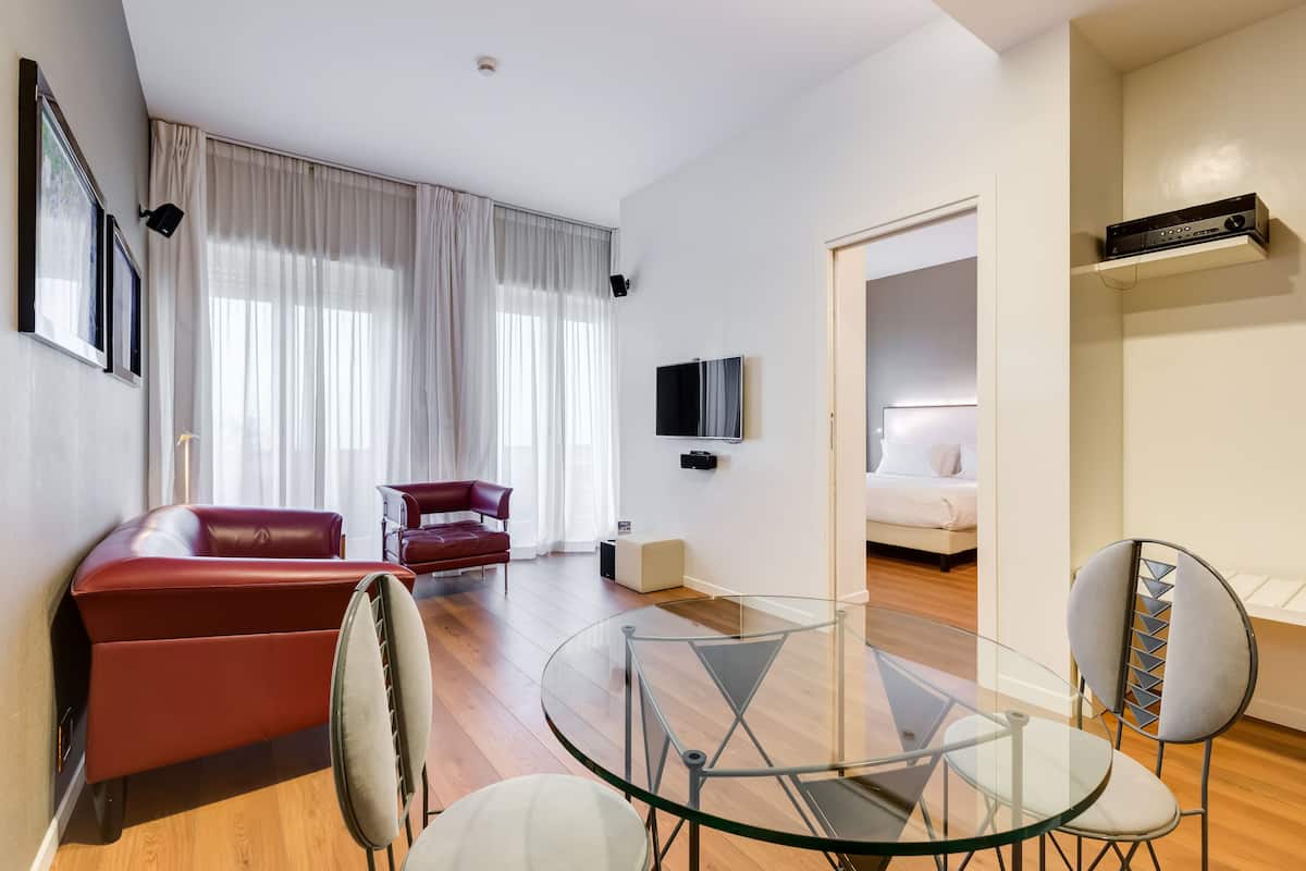 A modern living room with a glass table, red sofa, and a TV mounted on the wall.