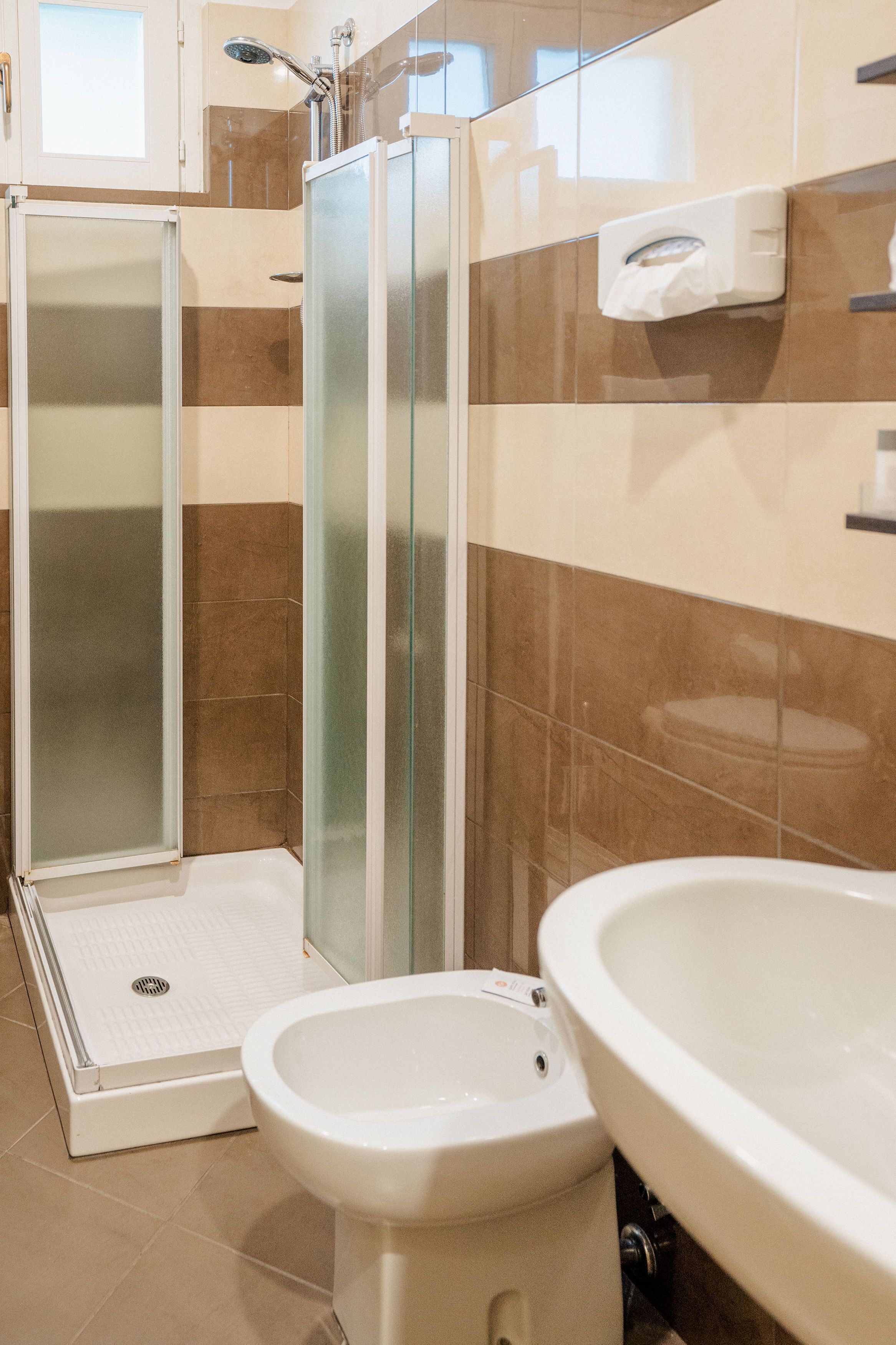 A bathroom with a glass shower enclosure, a bidet, and a sink.