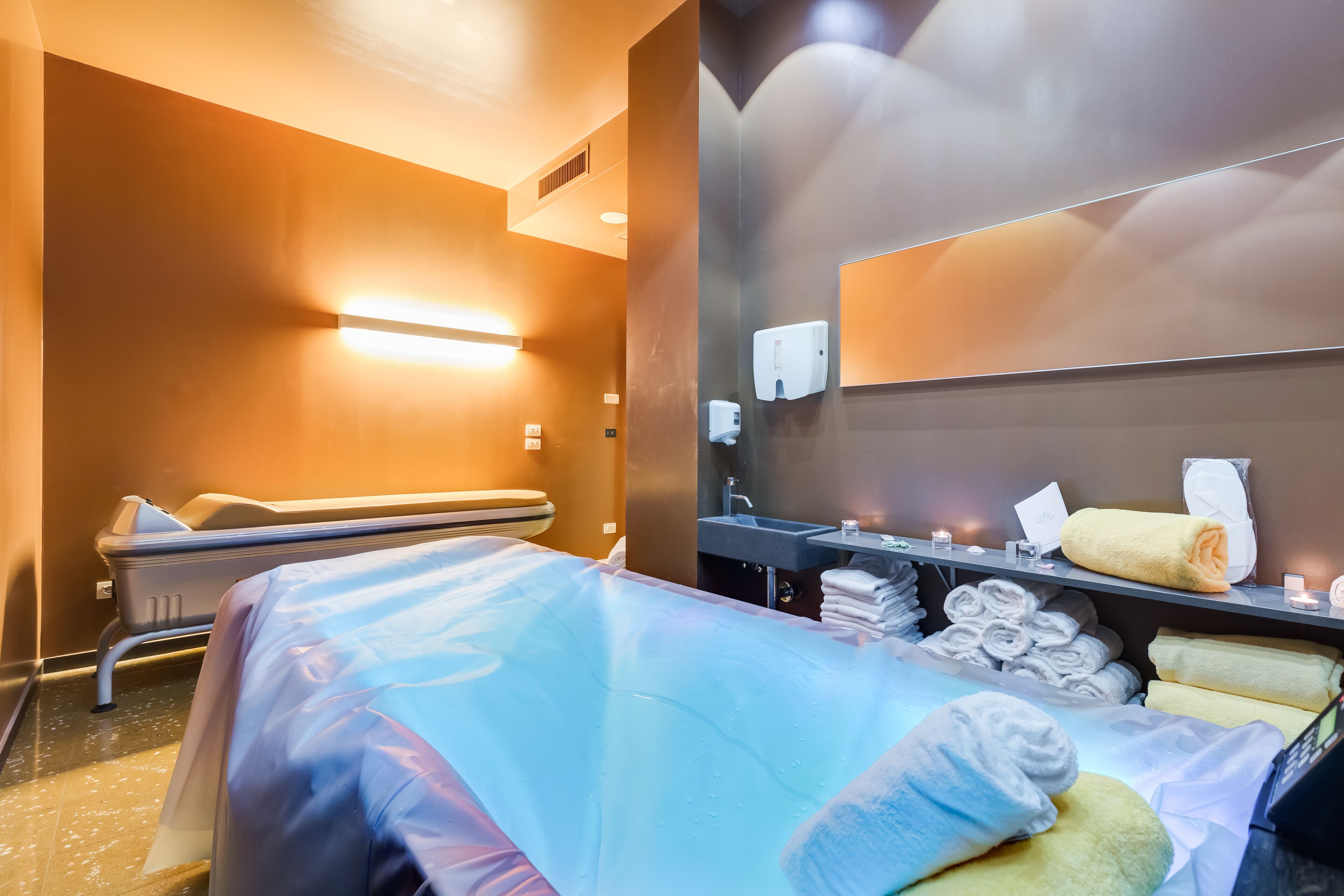 Habitación de hotel con cama, sillón de masajes, lavamanos y toallas.