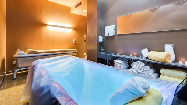 Une chambre d’hôtel équipée d’un lit, d’un fauteuil massant, d’un lavabo et de serviettes.