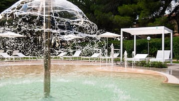 A water fountain with a dome structure, surrounded by a pool and lounge chairs.