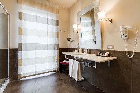 Un baño moderno con ducha, tocador con espejo, secador de pelo y teléfono.