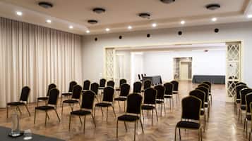 Un salón de conferencias con filas de sillas, una mesa con mantel y una cortina a un lado.