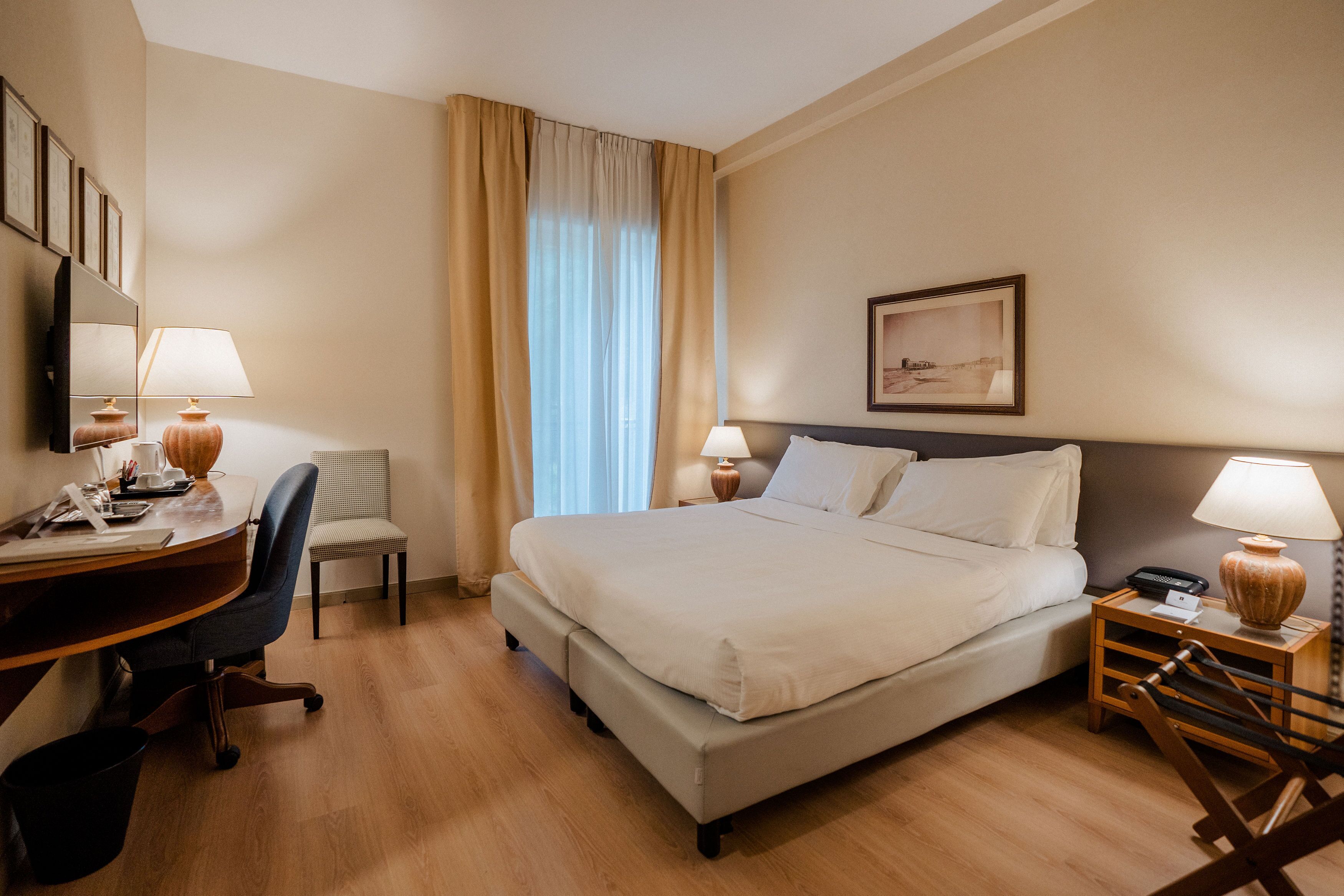 A hotel room with a bed, desk, chair, and bedside tables.