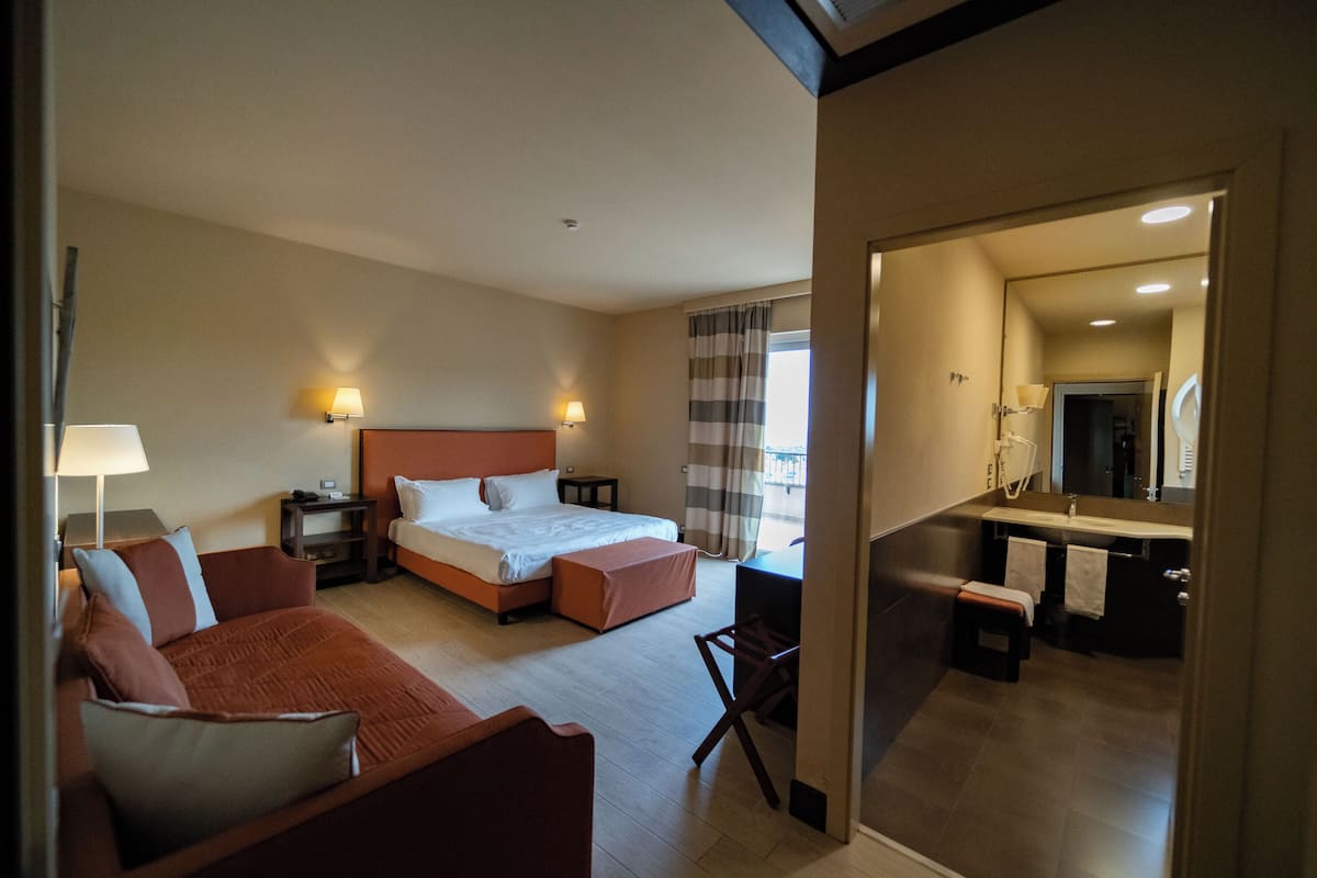 A hotel room with a bed, a sofa, a desk, and a bathroom with a mirror and sink.