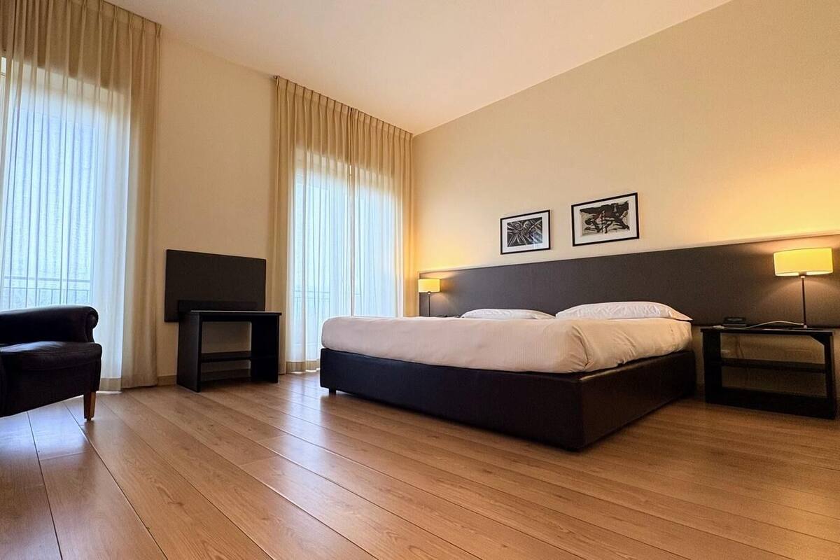 A hotel room with a bed, a chair, a TV, and two bedside lamps.