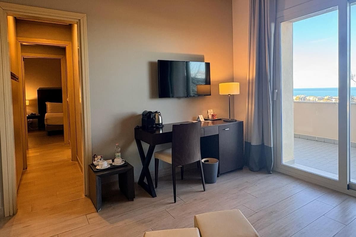 A hotel room with a desk, chair, TV, and a view of the sea.