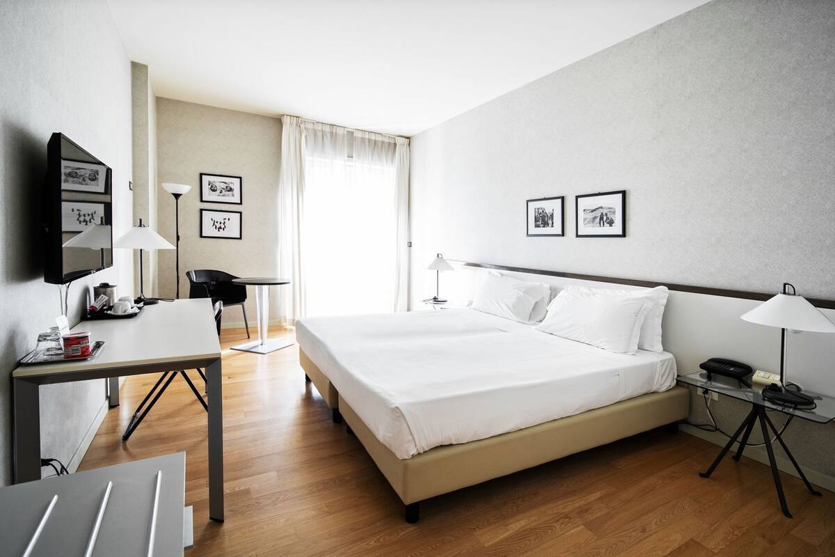 A hotel room with a bed, desk, chair, and a TV.