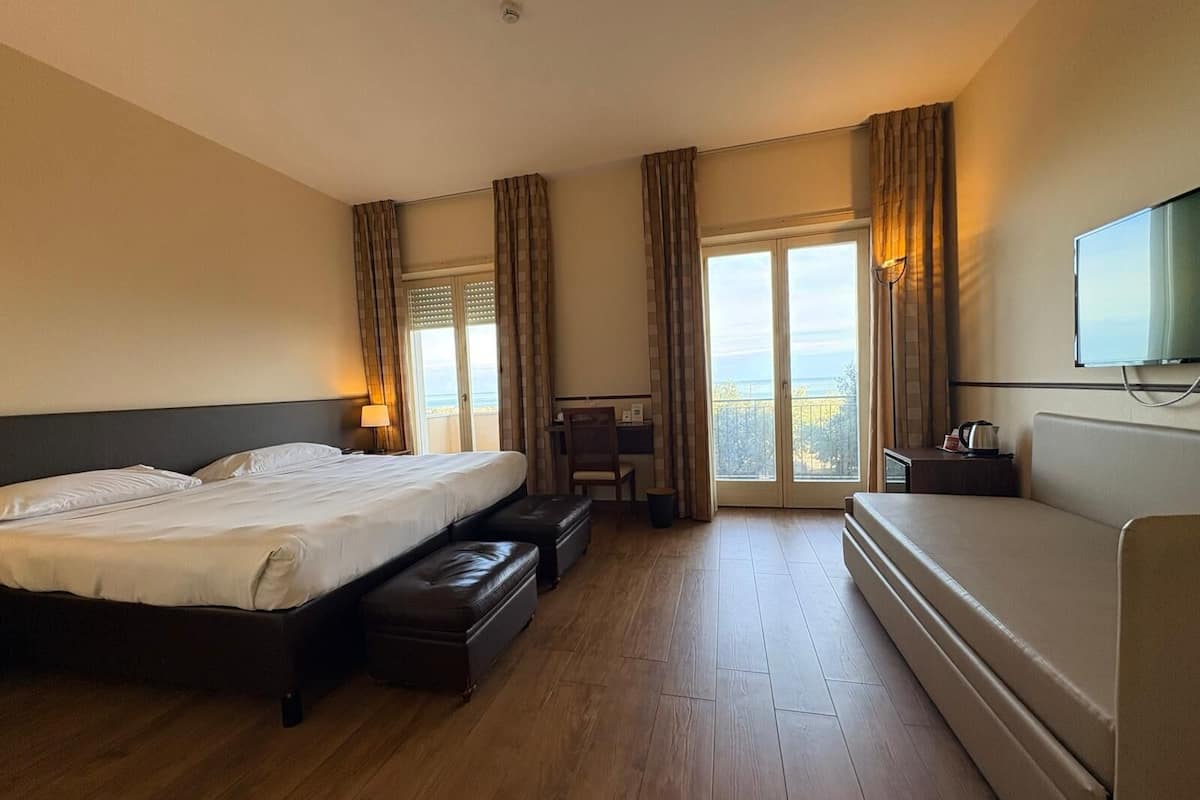 A hotel room with a large bed, a sofa, a desk, and a TV.