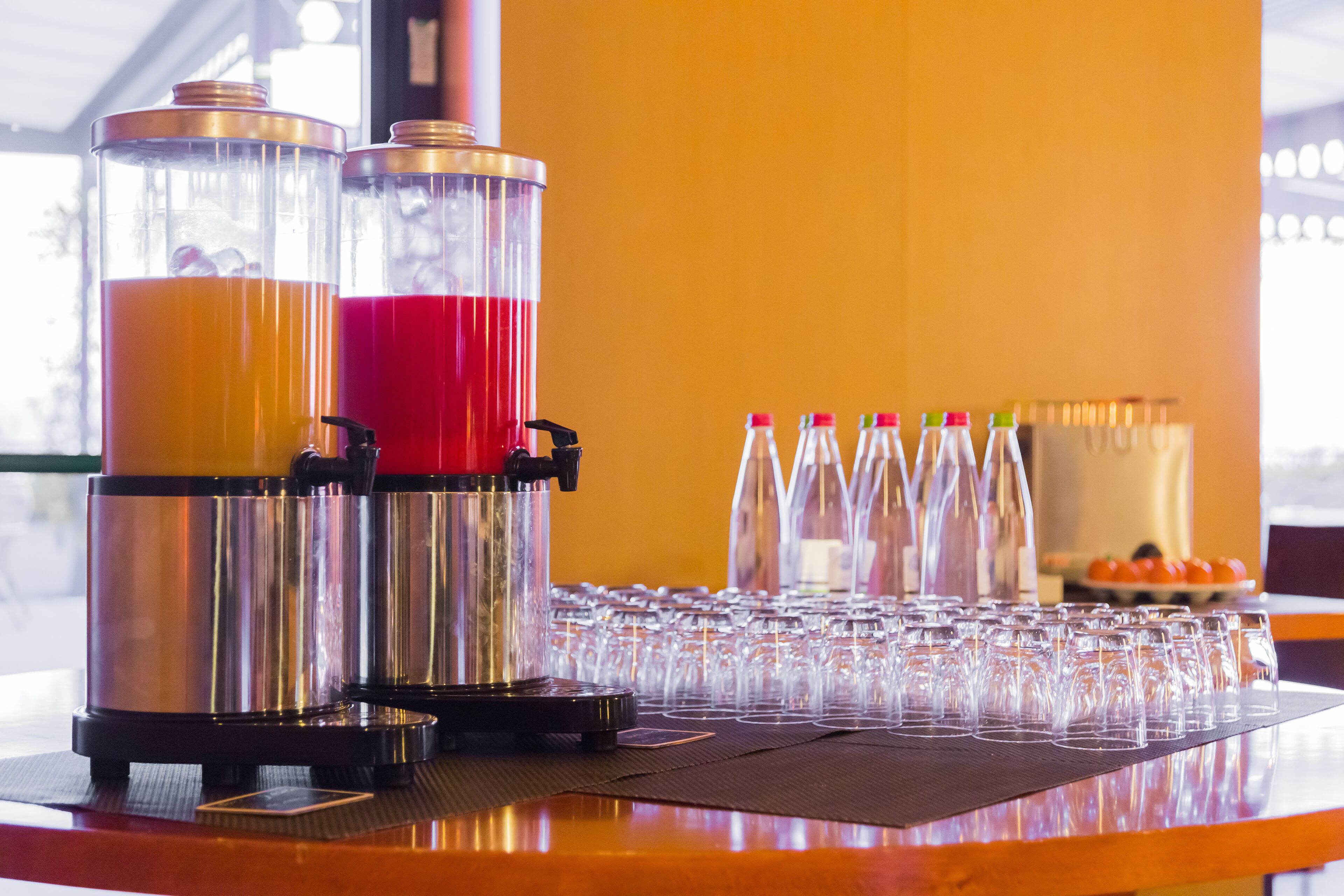 A bar area with two beverage dispensers, a row of glasses, and a fruit bowl in the background.
