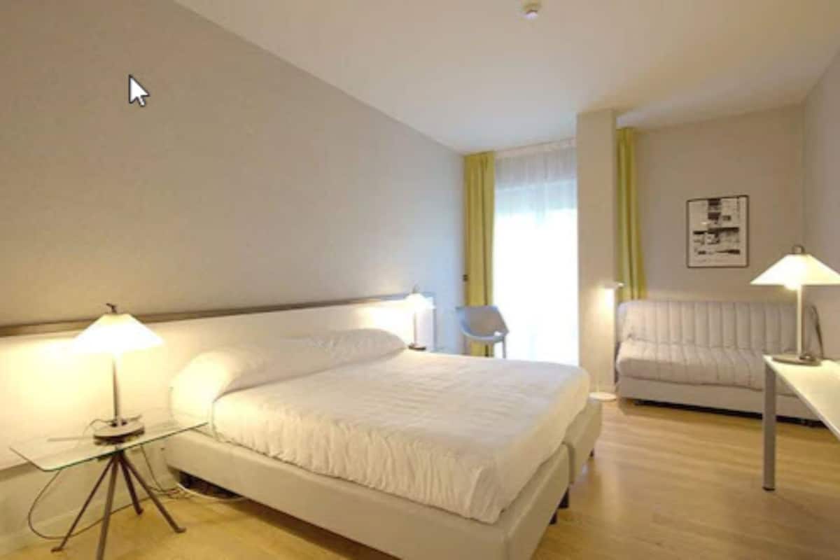A hotel room with a large bed, a desk, a chair, and a sofa.