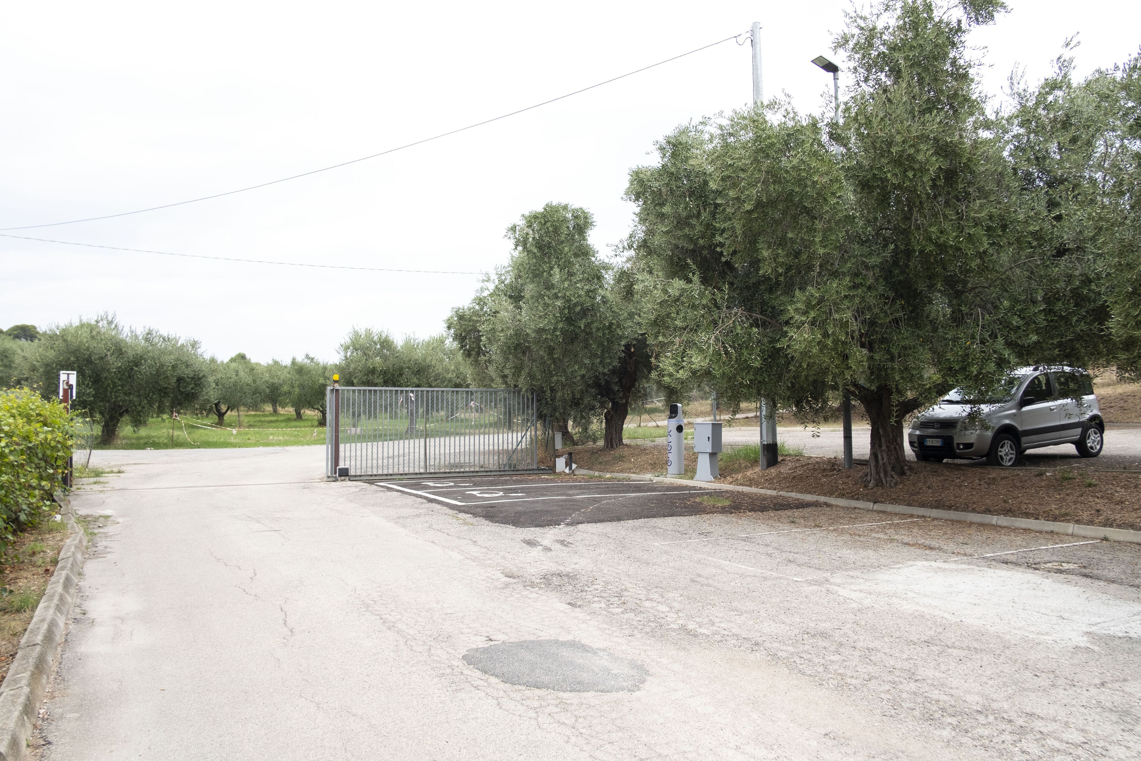 A gated parking area with a paved road, a metal fence, and a parked car.
