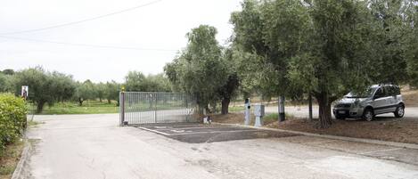 A gated parking area with a paved road, a metal fence, and a parked car.