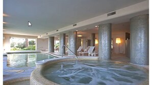 A hot tub area with tiled flooring, lounge chairs, and pillars.