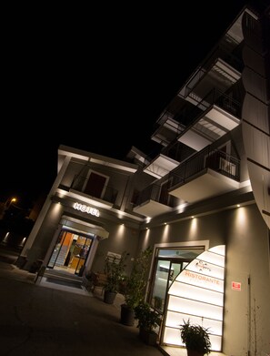 A modern hotel with a glass facade, outdoor seating area, and a sign for a restaurant.