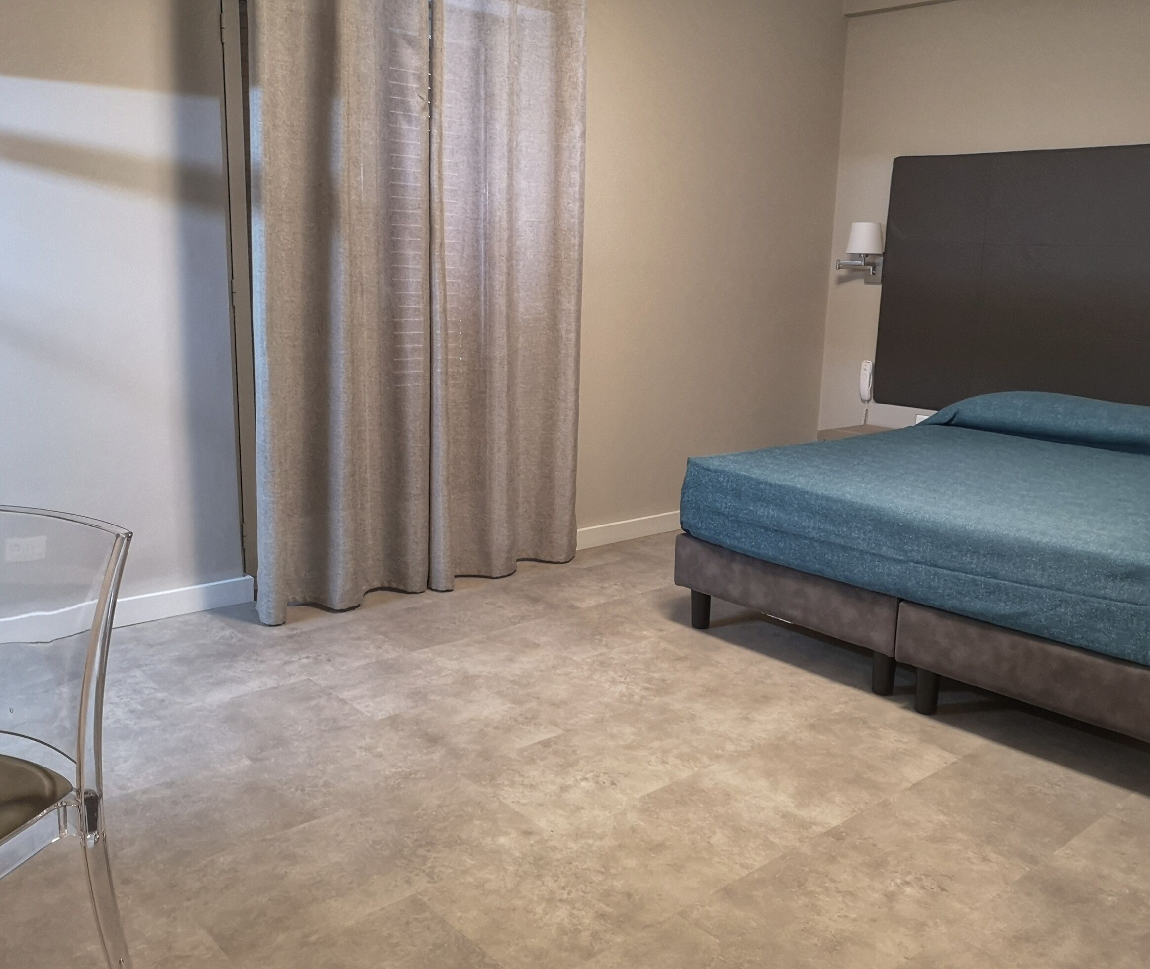 A bedroom with a bed, a chair, a curtain, and a wall-mounted lamp.