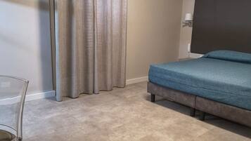 A bedroom with a bed, a chair, a curtain, and a wall-mounted lamp.