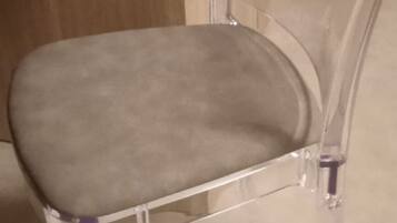 Una sedia trasparente in plastica con seduta e schienale imbottiti, posizionata su un pavimento rivestito di moquette.