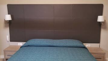 Een slaapkamer met een donker hoofdbord, een blauwgroene bedsprei, twee nachtkastjes en wandlampen.