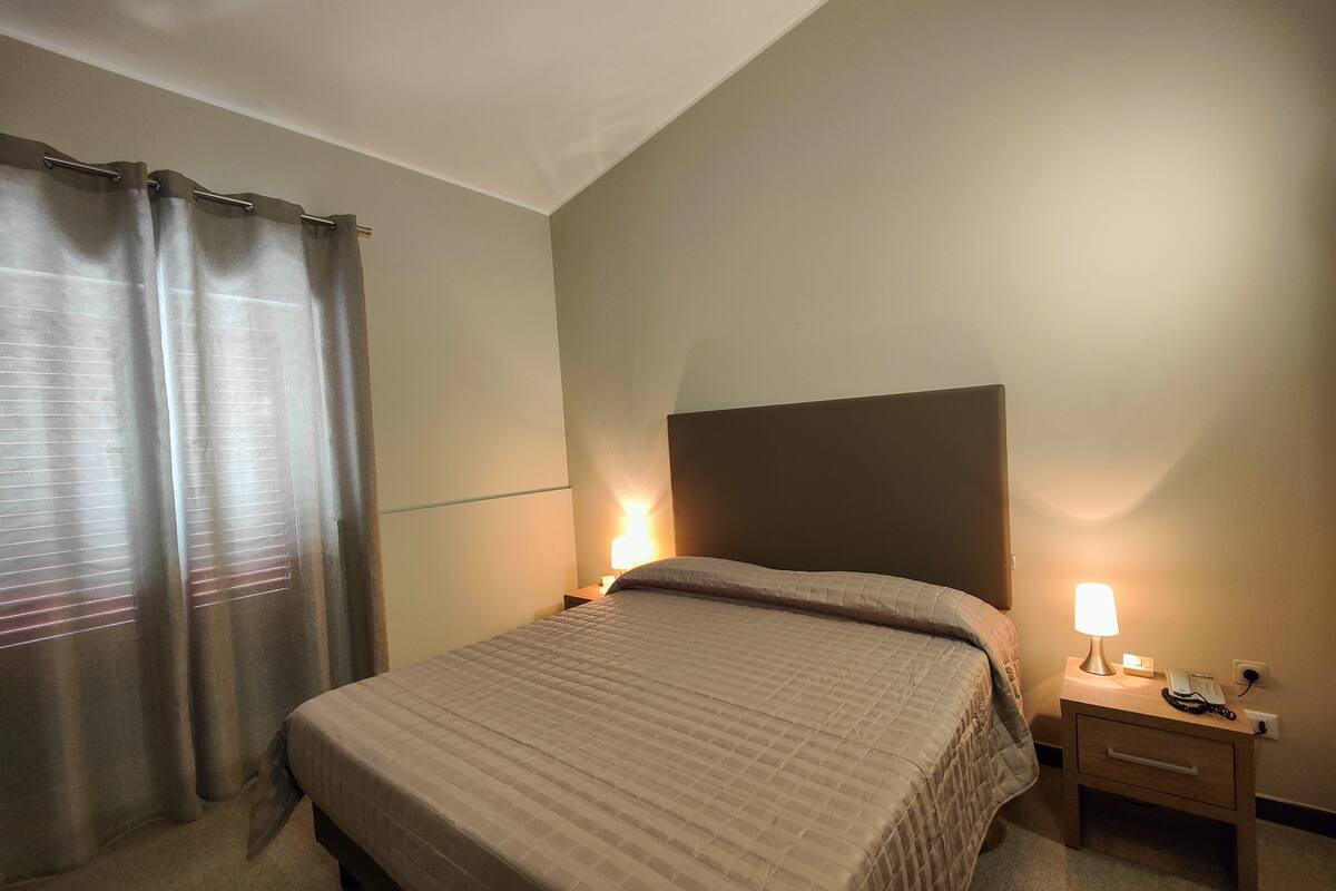 A hotel room with a bed, a nightstand with a lamp, and a window with curtains.