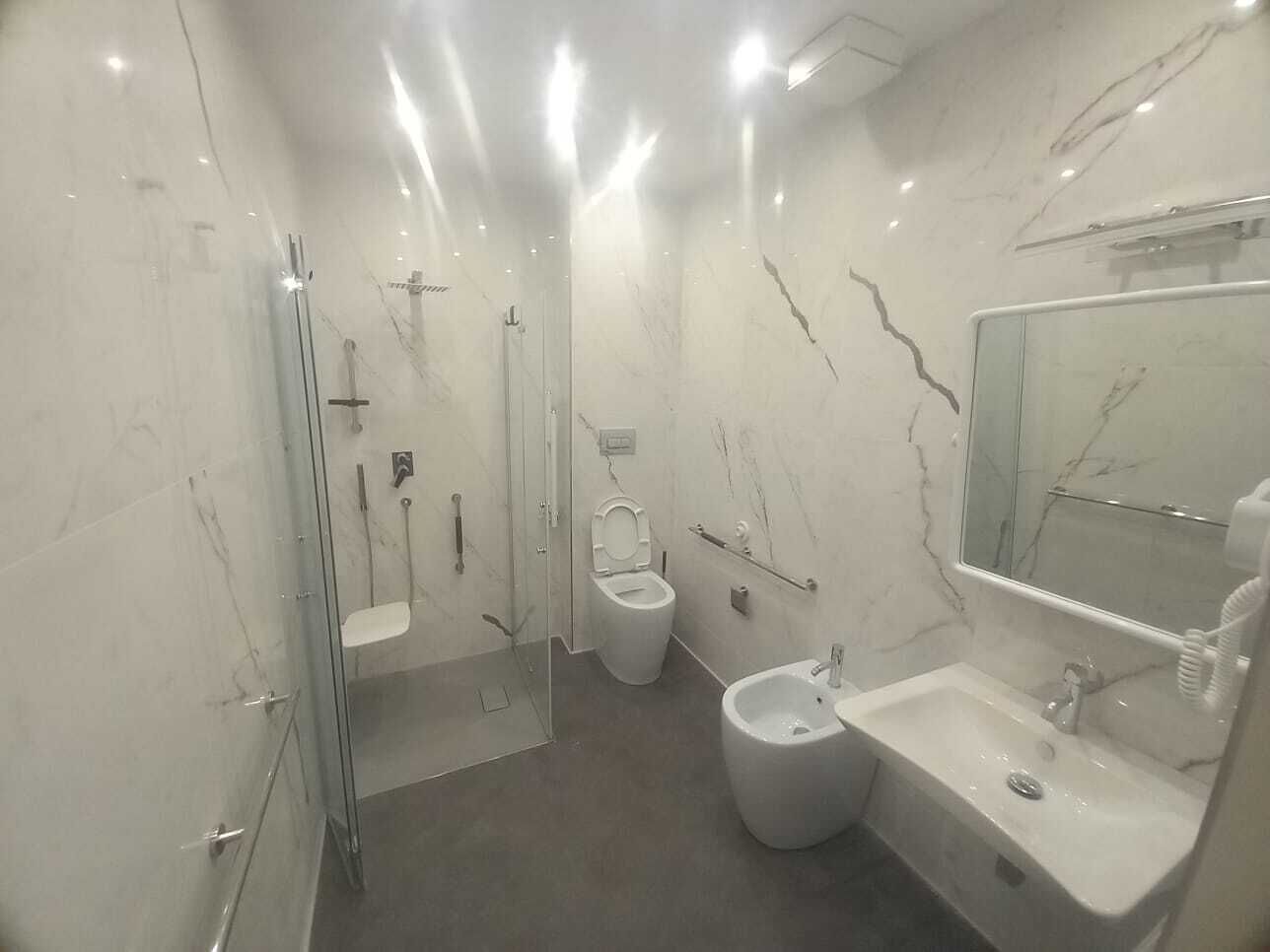 A modern bathroom with a glass-enclosed shower, a toilet, and a sink with a mirror.