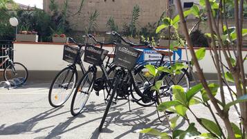 A row of bicycles with 'Il Gabbiano Hotel' branding and 'Bike Service' information, parked in front of a building with a sign reading 'Parchergo Riservato agli Alieni'.